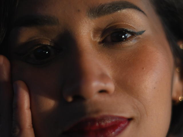 ScarlethFely's face, focusing on her dark eyes with black eyeliner, slightly parted red lips, and soft brown skin. Her hand rests on her cheek, shadowing her face.