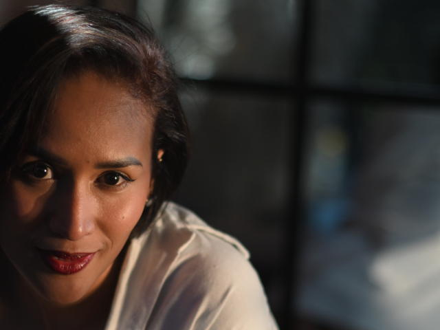 ScarlethFely's face with dark brown hair, slightly parted lips, red lipstick, and brown eyes, wearing a white shirt, illuminated by soft light, looking forward with a subtle smile.