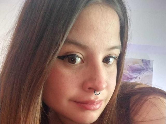 Melani Becker heeft bruine ogen, lang bruin haar, een neusring en glanzende, roze lippen. Haar wimpers zijn dik en ze glimlacht lichtjes. Haar huid is licht en ze is schattig..