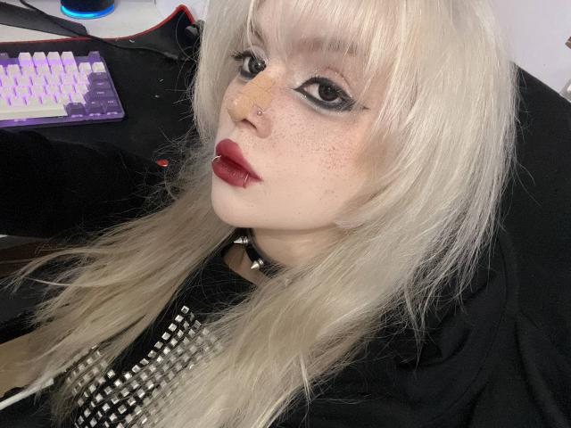 Carmelia Pratten a la peau pâle, des taches de rousseur et des cheveux blonds platine. Elle porte un eye-liner noir, du rouge à lèvres rouge, une chemise noire cloutée et un collier ras du cou noir. Elle a également un anneau au nez..