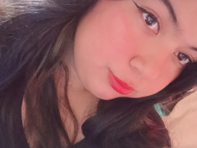 SultanaLm has pink blushed cheeks, long black hair, and red lipstick. She's looking at the camera with subtle eyeliner and a gentle smile. Her tits aren't visible.