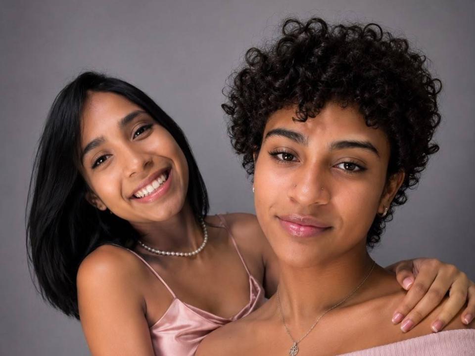 Valeryanddarianny with black straight hair and small tits, smiling, wearing a pink satin dress, arms around curly-haired Valeryanddarianny, who has a necklace and pink lips.