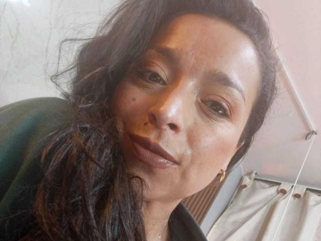 StangelarRivera ha la pelle marrone media, i capelli neri ondulati, un trucco leggero e una piccola lentiggine sulla guancia destra. Indossa una maglietta verde e orecchini dorati..
