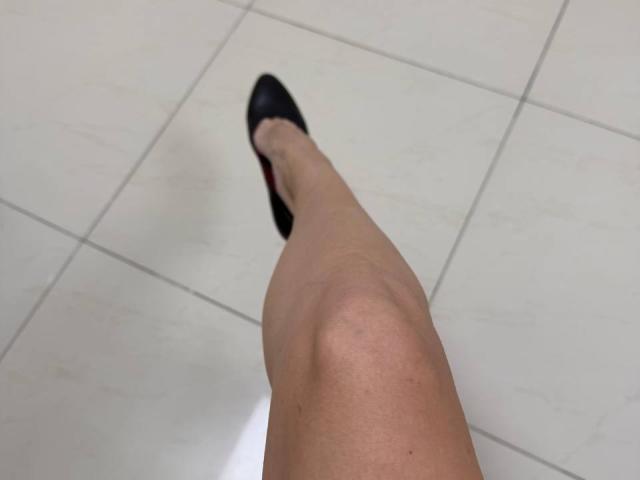 MoonLiza's leg, extending from the bottom left, wearing a black shoe, with a slightly visible knee and pale skin, on a white-tiled floor.