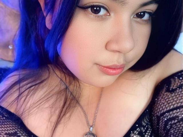 SultanaLm tiene una cara linda con ojos oscuros, labios rosados y cabello negro. Lleva una blusa de malla negra que deja ver sus senos, y un collar con un dije..