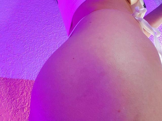 Il sedere di SofiaSpring è al centro dell'attenzione, mostrando una pelle liscia e chiara, con una leggera abbronzatura, illuminata da luci viola e rosa, e indossa biancheria intima bianca con un dettaglio arricciato su un lato..