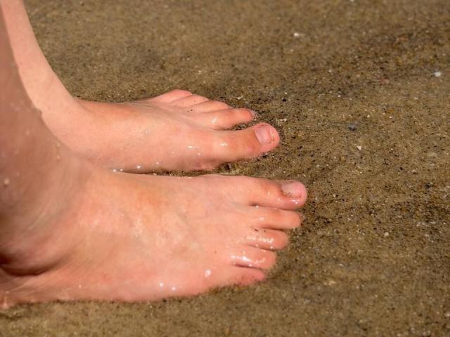 Les orteils sablonneux de Marriam, légèrement mouillés par l'eau, avec de minuscules grains accrochés à sa peau. Ses orteils roses sont pointus, et ses orteils sont légèrement écartés sur la plage..