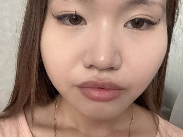 El rostro de DirtyAsianLunachka, mostrando una piel brillante, ojos marrones con pestañas largas, labios rosados y cabello castaño lacio, vestida con una blusa rosa y una cadena dorada, en un selfie..