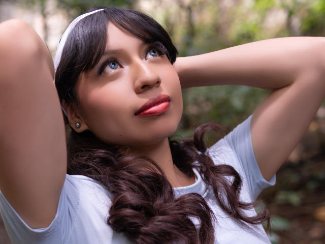 ZoeRedds has blue eyes, brown curly hair, white headband, and pink lips, wearing a white shirt, arms raised, looking up with a slight smile. Boobless, no visible pussy.