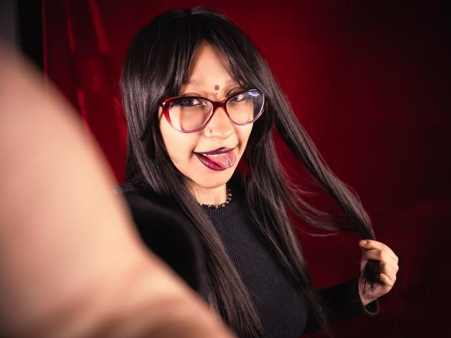 JinXkm has long black hair, red glasses, and a black top, sticking out her tongue with a playful expression, holding her hair with a focused, slightly blurred foreground.