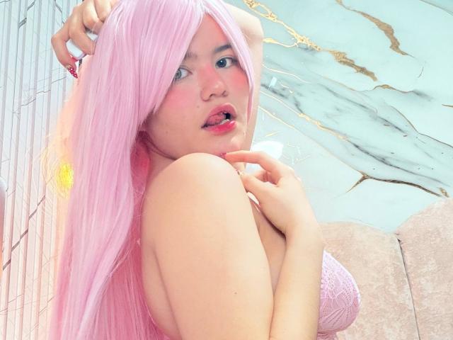 AlexaMissFortune with pink hair, looking back, pink lips, blushed cheeks, hand on head, pink lace bra, showing tits, pink nails, soft lighting, slightly open mouth, sexy pose.
