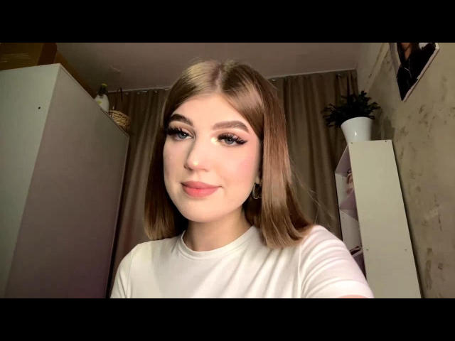 Tawanna Lehrman, mit schulterlangem braunen Haar, weißem Hemd, pinkem Lippenstift und langen Wimpern, lächelt in die Kamera und zeigt ihre Brüste und ihre pinke Vulva..