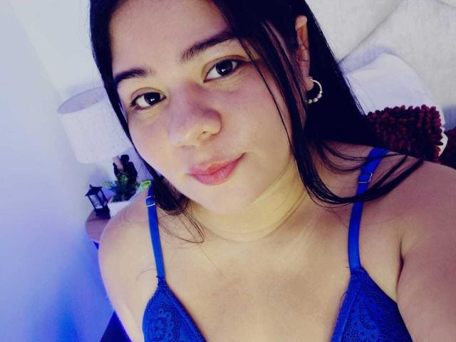 ElizaWiliamst with medium tits in a blue lace bra, long black hair, hoop earrings, light skin, subtle smile, and soft makeup, lying on a bed in a relaxed pose.