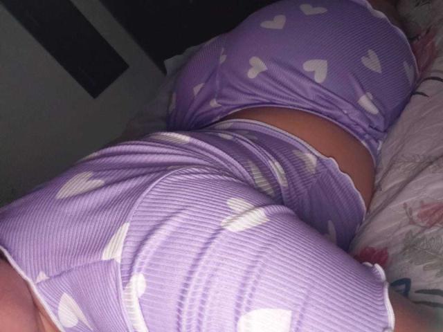 ElizaWiliamst lying on her side in purple ribbed pajamas with white heart patterns, showing her big ass and small, tight waist. Her back is slightly arched.