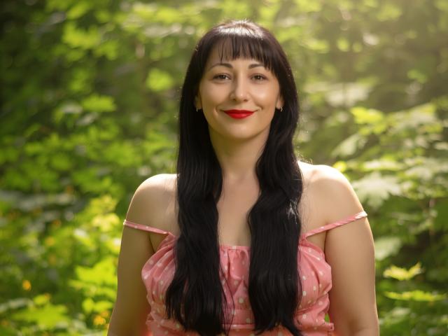LiluGrants has long black hair, red lipstick, and a pink polka-dot top with off-shoulder straps, smiling with her tits slightly visible, standing in a sunlit forest.
