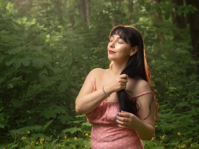 LiluGrants with long black hair, pink polka-dot dress, and red lipstick, standing in a forest, eyes closed, smiling, touching her hair, sunlight filtering through.