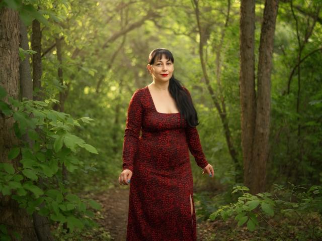 LiluGrants mit schwarzem Pferdeschwanz, trägt ein rotes und schwarzes Leopardenmuster-Kleid, steht im Wald, hat roten Lippenstift, mittelgroße Brüste und ein süßes Gesicht und blickt leicht zur Seite..