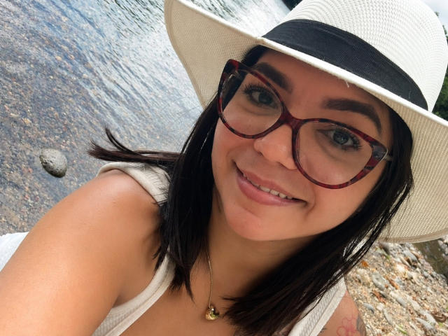 ValeryPierce with glasses, white hat, black hair, smiling, tan skin, small nose, wearing a white tank top, necklace with gold pendant, visible tattoo on right shoulder.