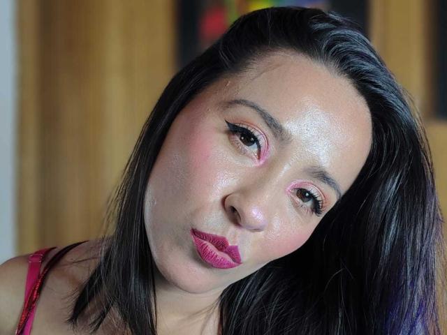 AgathaTeranh has shiny skin, pink eye makeup, black straight hair, and pink lipstick, pouting slightly with a cute, playful expression. Her tits are not visible.
