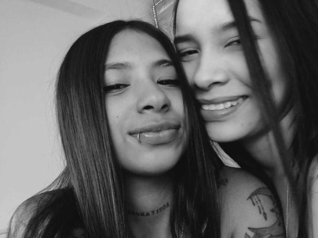 Black-and-white selfie of DakotaandJuliette, both with long hair. DakotaandJuliette on the left has a lip piercing and a necklace, smiling with closed eyes. Tattoo on right shoulder.