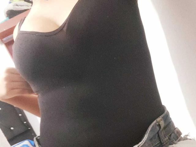 Le débardeur noir de BonnieBodn, qui révèle ses petites seins et un aperçu de l'élastique de son jean, avec une main qui tire sur le haut. Sa peau est claire..