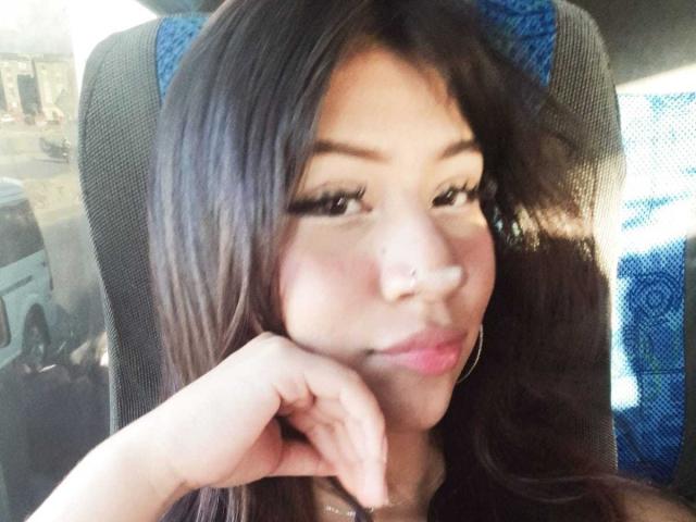 BonnieBodn, avec de longs cheveux bruns, un anneau au nez et des boucles d'oreilles, appuyant son menton sur sa main, souriant légèrement, assise dans une voiture avec un siège bleu..