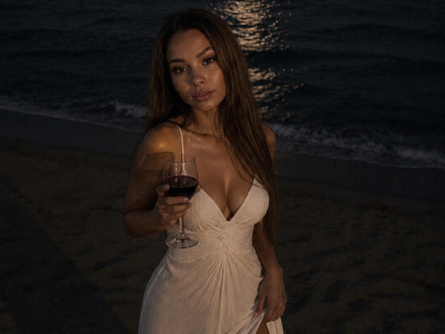 Niferttiti with long brown hair, wearing a white dress, holding a glass of red wine, standing on a dark beach at night, looking directly at the camera.