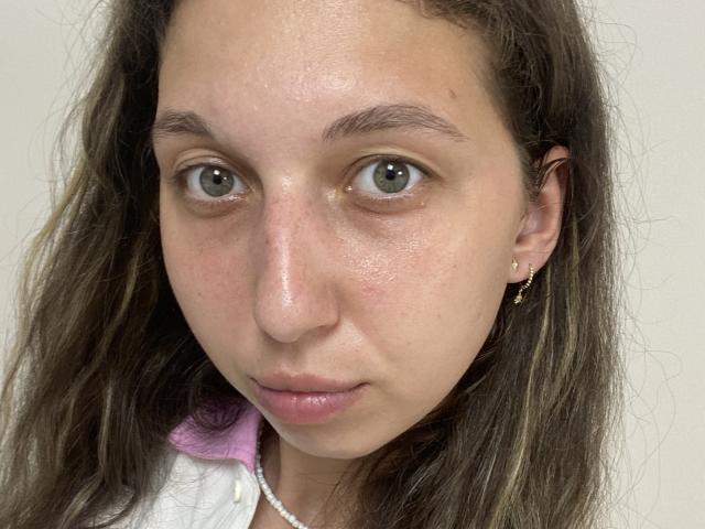 Sanella's face has light brown eyes, slightly wavy brown hair, pinkish lips, and a small nose. She wears a pearl necklace and a gold earring on her right ear.