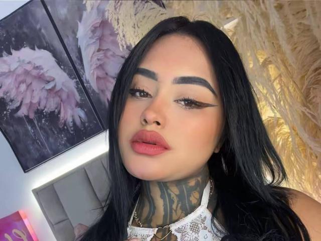 LairaHearvy has black hair, thick eyebrows, and pink lips. She's wearing lace and has tattoos on her neck. Her makeup is bold with winged eyeliner. Boobs not visible.