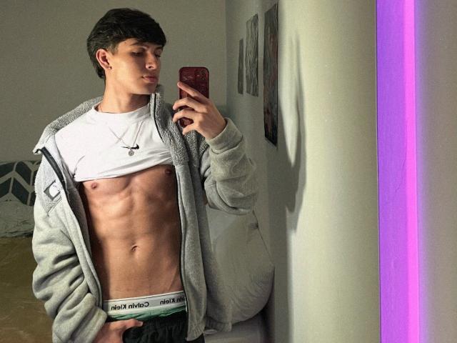 Angelitocute with a lean, muscular, abs-visible body, wearing a gray zip-up, white tee, and Calvin Klein underwear, taking a mirror selfie with a red phone.