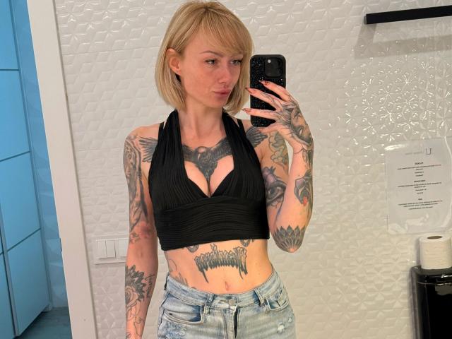HaileyhopeXXX-hot with blonde bob, black halter top, tattoos on arms, chest, and stomach, wearing faded jeans, taking a mirror selfie, showing her tits and a toned, sexy body.