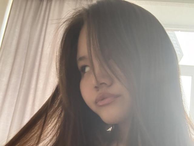 DirtyAsianLunachka has long brown hair covering one eye, slightly parted pink lips, and a small nose. She's looking to the side with a soft, playful expression.