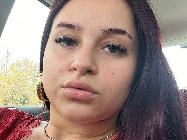 Luucie heeft volle, roze lippen, dikke zwarte wimpers en lichtrode wangen, draagt gouden oorbellen en een rood gestreept shirt, met bruin haar en een klein sproetje op haar neus..