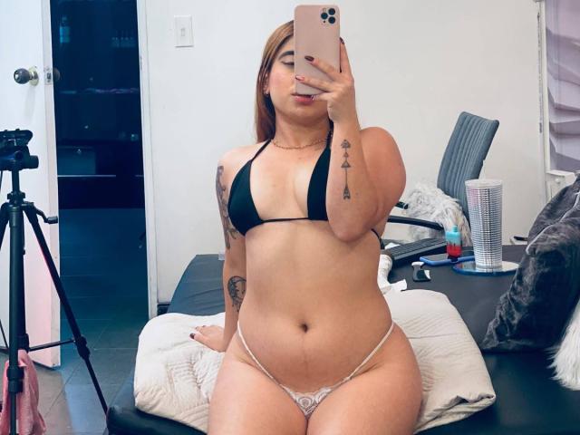 MartinaConnorr is taking a selfie in a mirror, wearing a black bikini top and white thong, exposing her tits and pussy, with tattoos on her arm and hand.