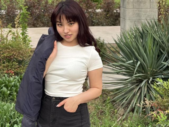 LeoraHardeman with dark hair, white ribbed shirt, black high-waisted pants, hand in pocket, holding navy jacket, standing in green garden, small butt, slim, cute, subtle smile.