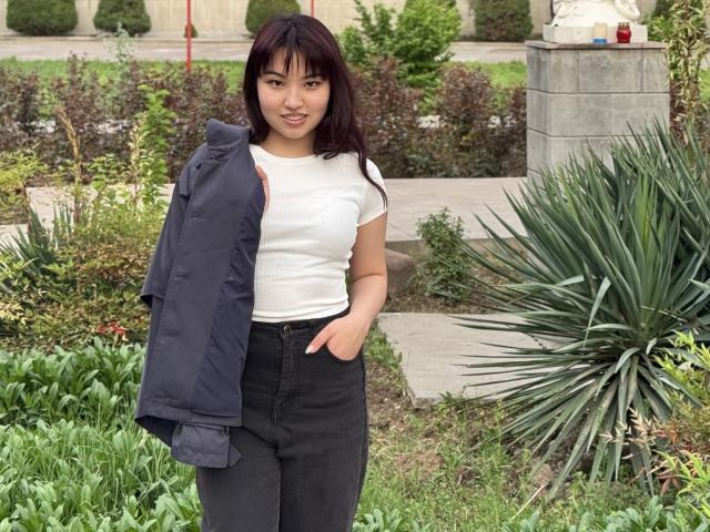 Leora Hardeman se tient dans un jardin, vêtue d'un t-shirt blanc, d'un jean noir et d'une veste marine qu'elle porte sur son épaule. Sa main est dans sa poche, elle a les cheveux foncés et un sourire..