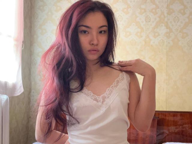 LeoraHardeman with long red-brown hair, wearing a white lace-trimmed camisole, standing in a room, hand on shoulder, looking at camera, light from window on left.
