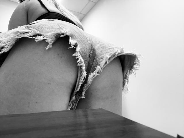 DiLaria's ripped, frayed denim shorts are hanging off her butt, showing her pale, slightly textured skin and a dark top. Shot from a low angle, focusing on her ass.