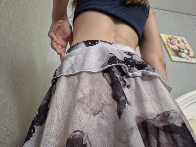 Seliina's bare midriff, wearing a black crop top and a flowy, floral-patterned skirt, standing with her ass facing the camera, hands on her hips, showing a toned back.