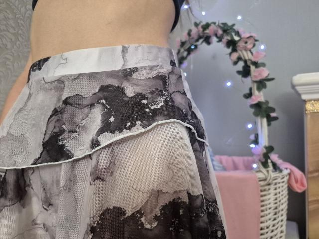 Seliina's ass, wearing a sheer black and white floral skirt, standing with her back to the camera. Her bare lower back is visible.