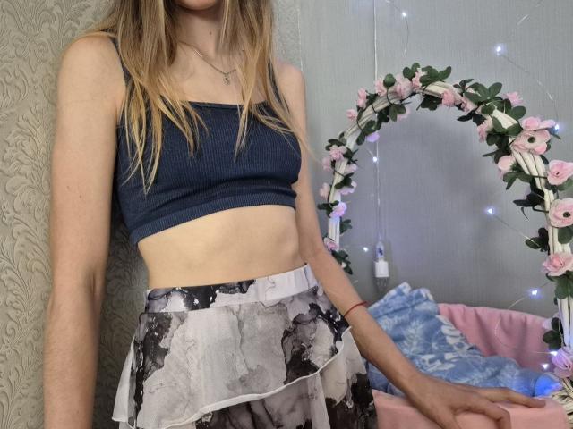 Seliina with a slim, pale body, small tits in a navy blue crop top, and a black and white ruffle skirt, standing near a pink flower arch.