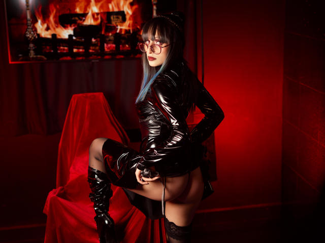 TatsumiLee in black latex dress, glasses, blue hair, thigh-high boots, exposing her bare ass while sitting on a chair, red lighting, fire wall in background.