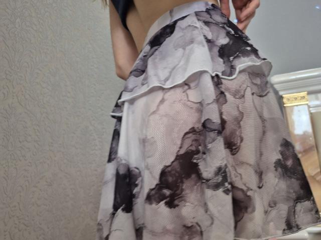 Seliina's ass in a sheer, ruffled, black-and-gray patterned skirt, showing a bit of white underwear, with her hand partially visible, in a slightly tilted, low-angle shot.