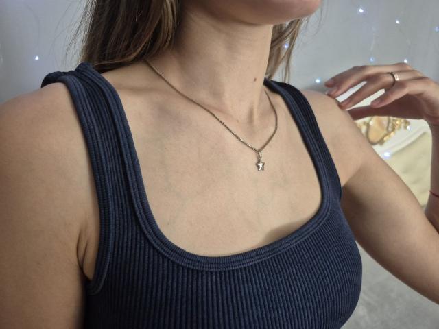 Seliina's chest with small tits, wearing a ribbed navy tank top, silver necklace, and a ring on her right hand. Her skin is light, and she has brown hair.