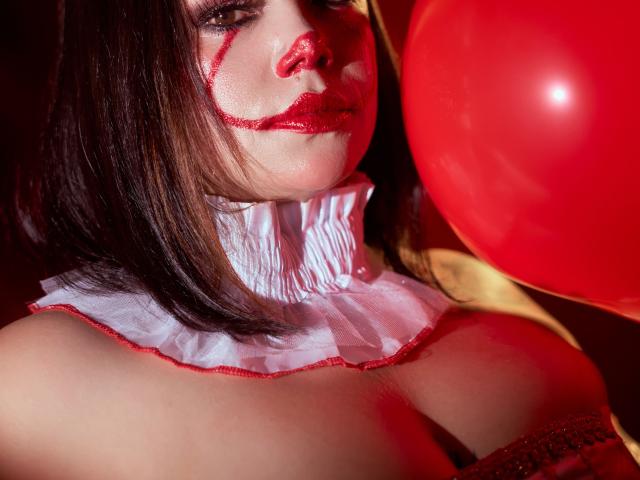 SamanthaVenus met rode lippenstift en make-up, die een rode ballon vasthoudt, met een witte, gerimpelde kraag, waarbij haar grote borsten zichtbaar zijn, met bruin haar, en een sexy, verleidelijke uitstraling..