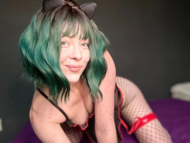JessieFire-hot with green wavy hair, black cat ears, pouty lips, and fishnet legs, wearing black and red lingerie, showing her boobs and ass, in a sexy pose.