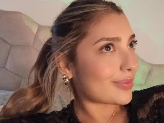 BiancaRey has tan skin, brown eyes, and a slight smile. She's wearing black lace, has a ponytail, and gold earrings with a ball design. Her tits are not visible.