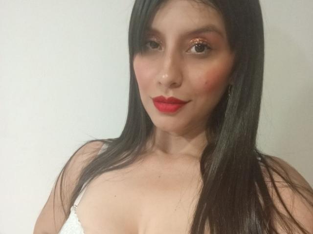 MadissonFontaine with long black hair, red lipstick, and subtle eye makeup, showing her bare shoulders and small tits in a white top. Soft smile, light skin, and gentle expression.