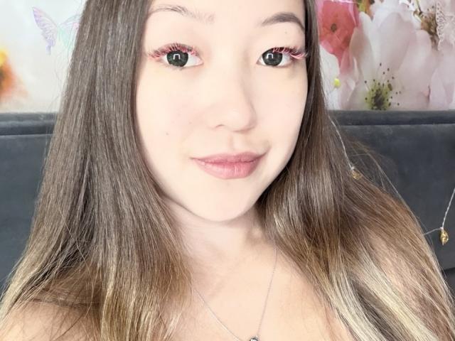 RenyLime has light skin, long brown hair with blonde tips, pink eyelashes, and pink lipstick. She's smiling with green eyes, and she's wearing a silver necklace.
