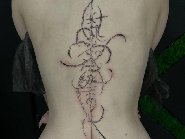 Het kale rug van Juliet Erbst, met een ingewikkeld zwart tattoo van gedraaide, wijnstokachtige patronen die verticaal lopen. De tattoo heeft roze, verhoogde huidgebieden in het midden..